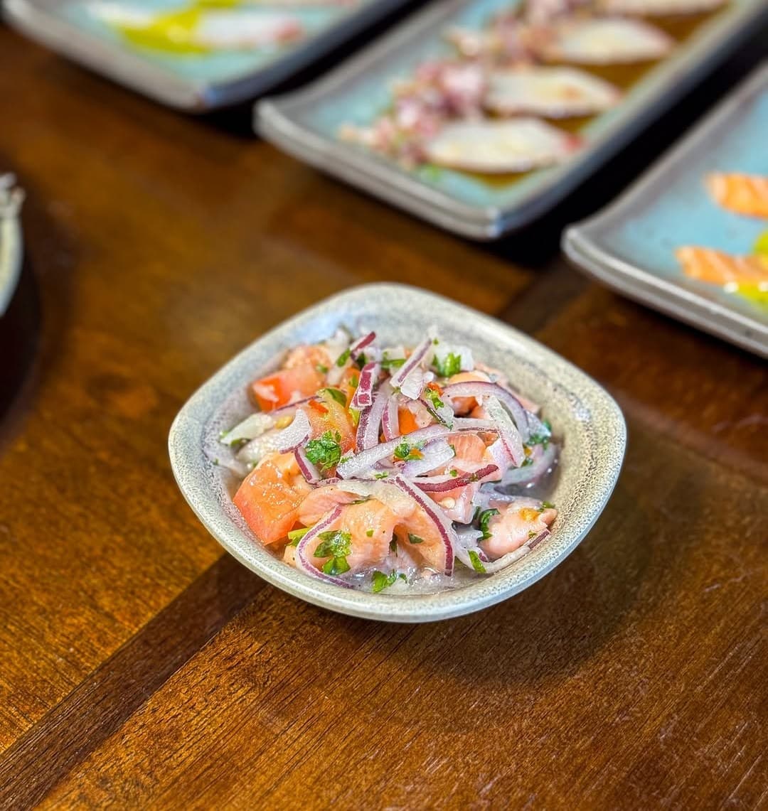 Ceviche de salmão numa tigela, com a mesa do rodízio ao fundo