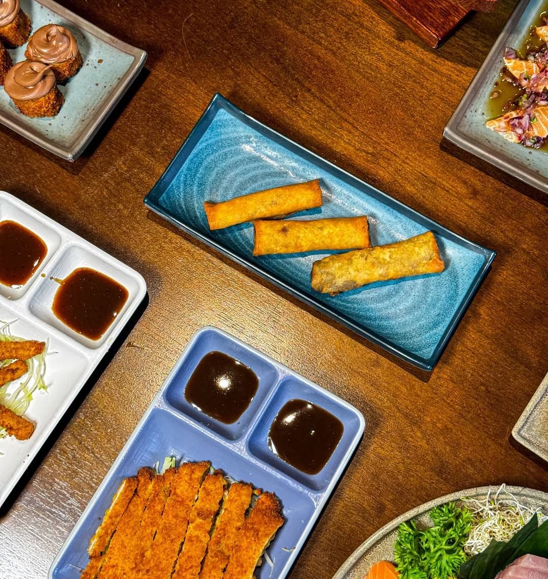 Chickenkatsu e harumakis em pratos azuis com molhos
