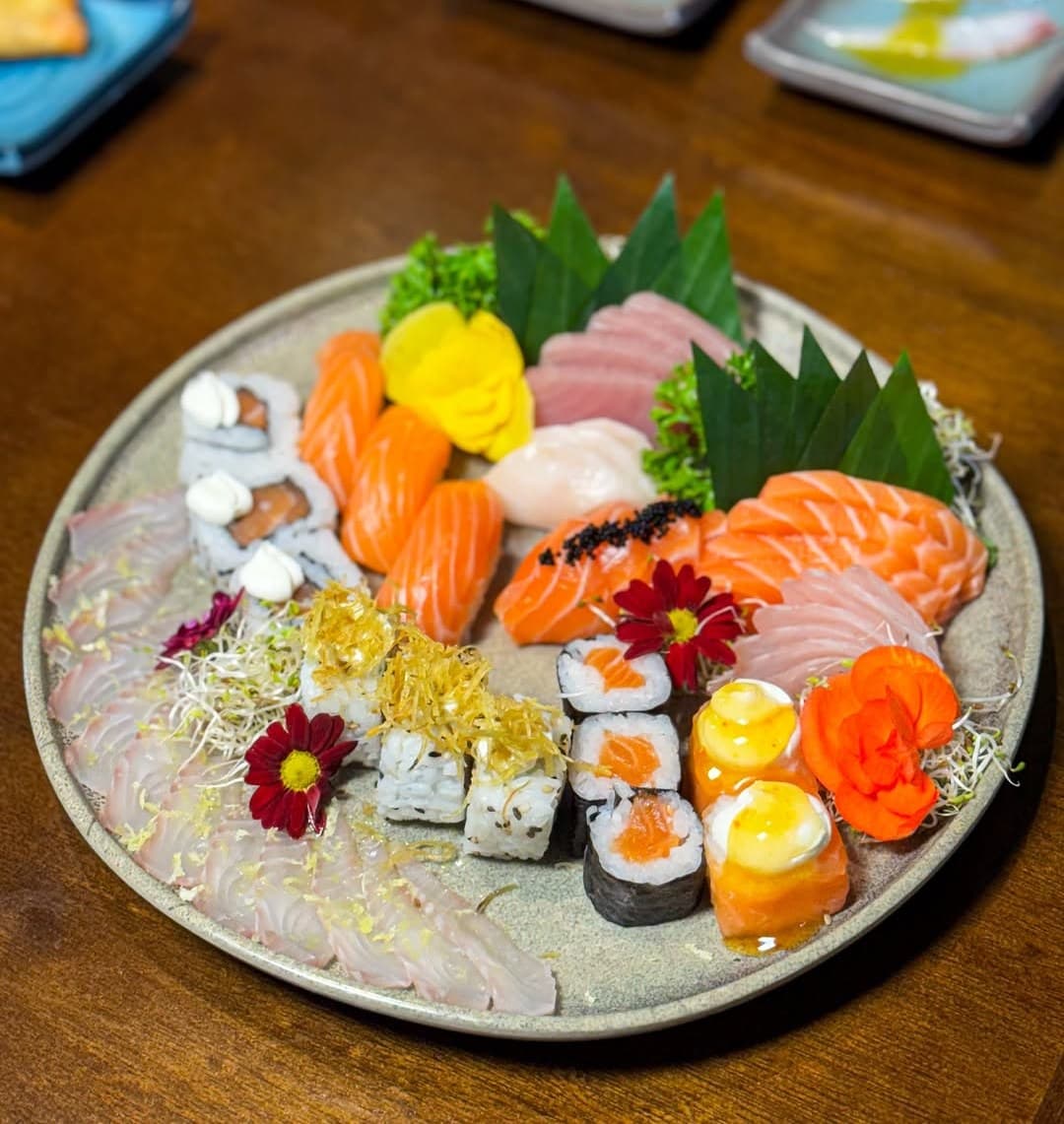 Combinado de sushis e sashimis com hashis, numa mesa de madeira