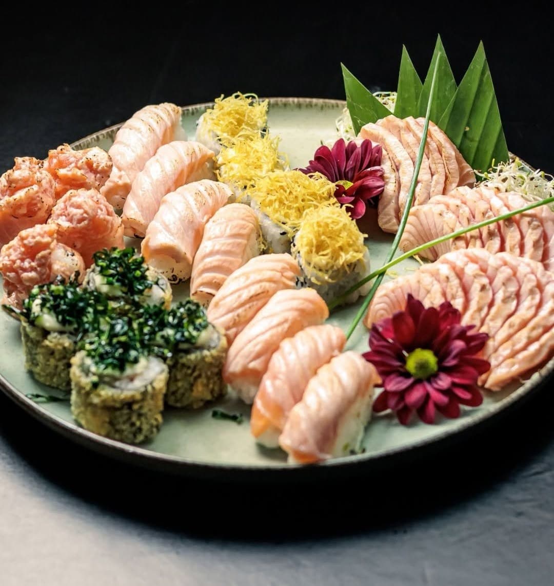 Combinado com nigiris de salmão maçaricado, hots e flores num prato, sobre fundo preto
