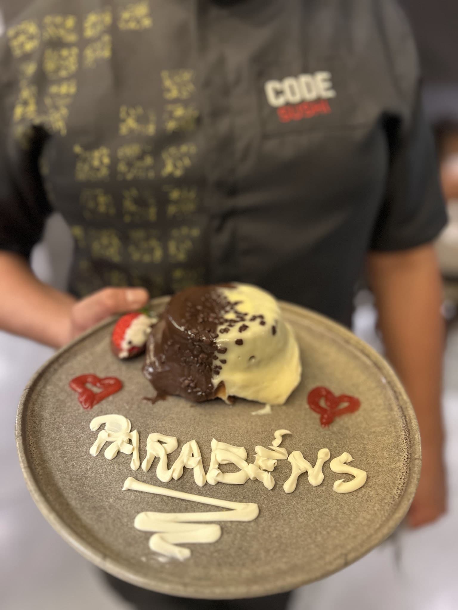 Sobremesa de aniversário com 'Parabéns' escrito no prato, servida pelo garçom