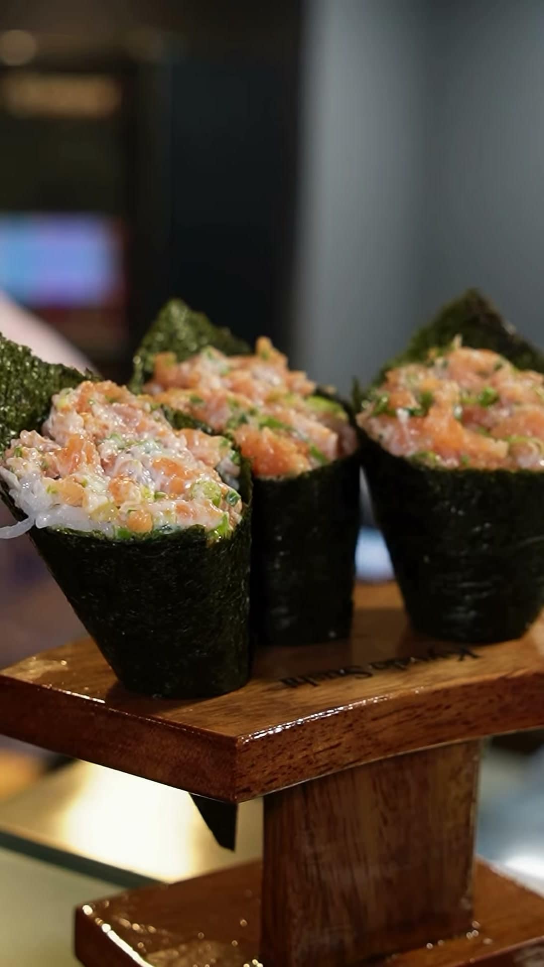Três temakis de salmão sobre um suporte de madeira, em luz baixa