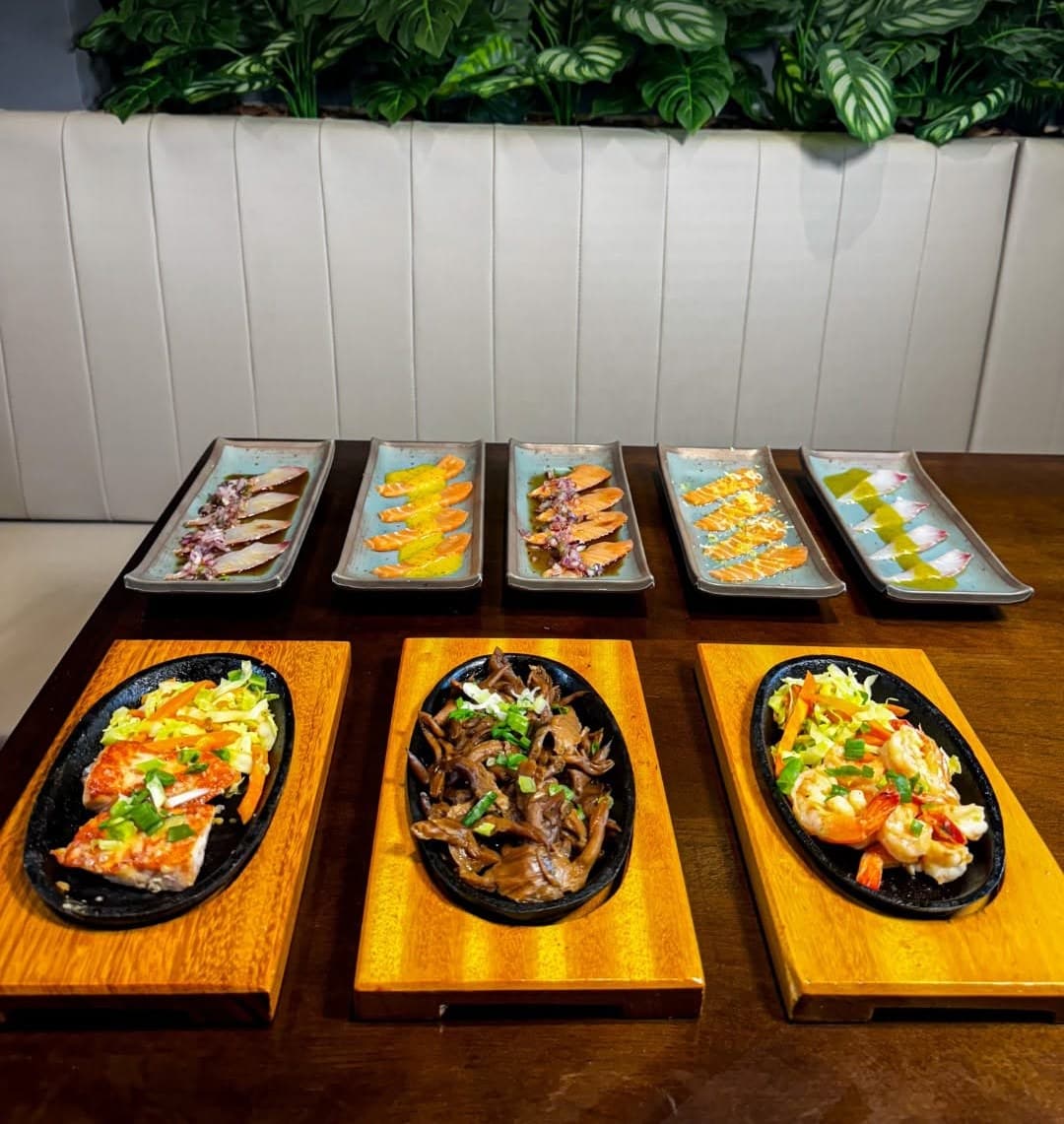 Mesa do rodízio com chapas, entradas e carpaccios junto à parede de plantas