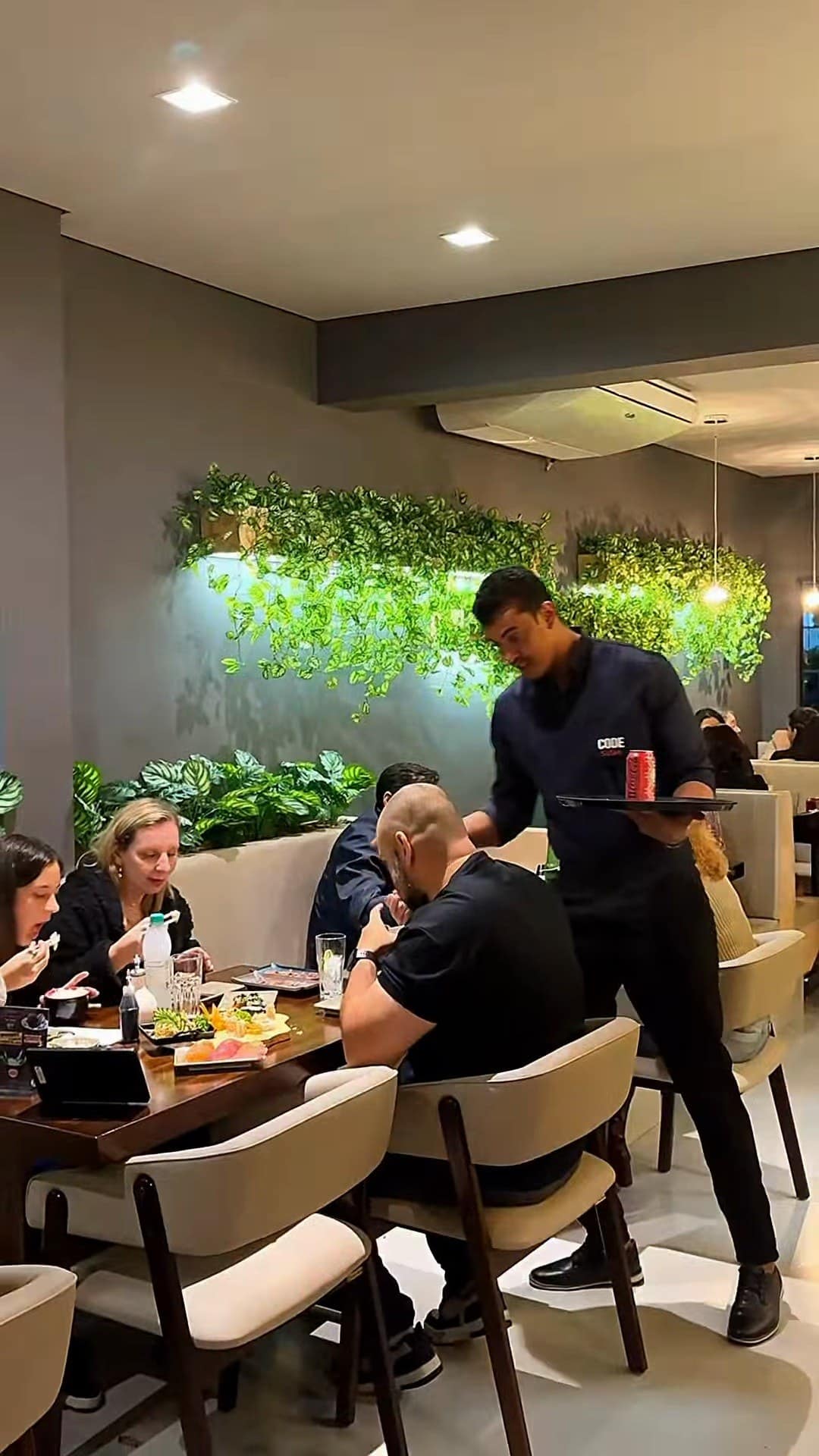 O salão à noite, com a parede de plantas iluminada e mesas cheias