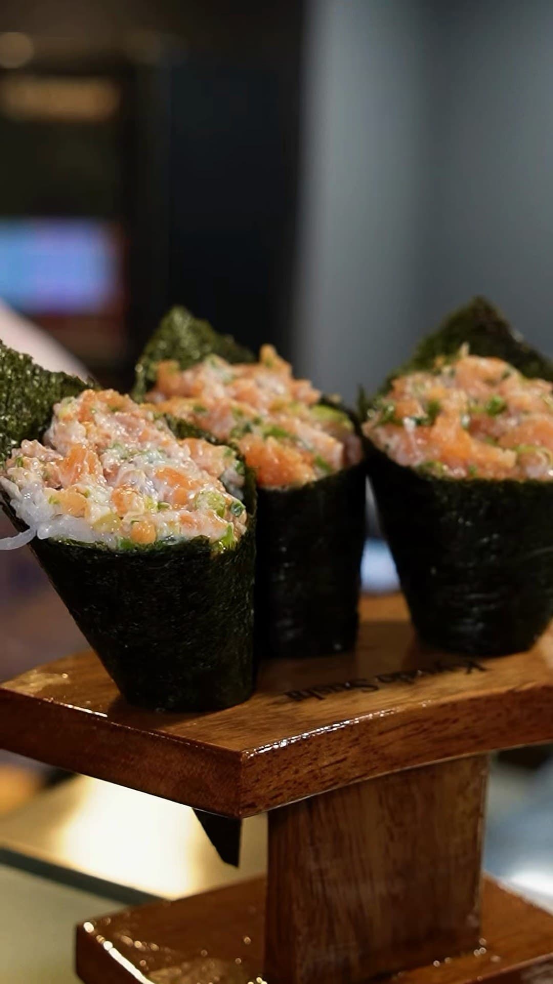 Temakis de salmão alinhados no suporte de madeira, em luz baixa