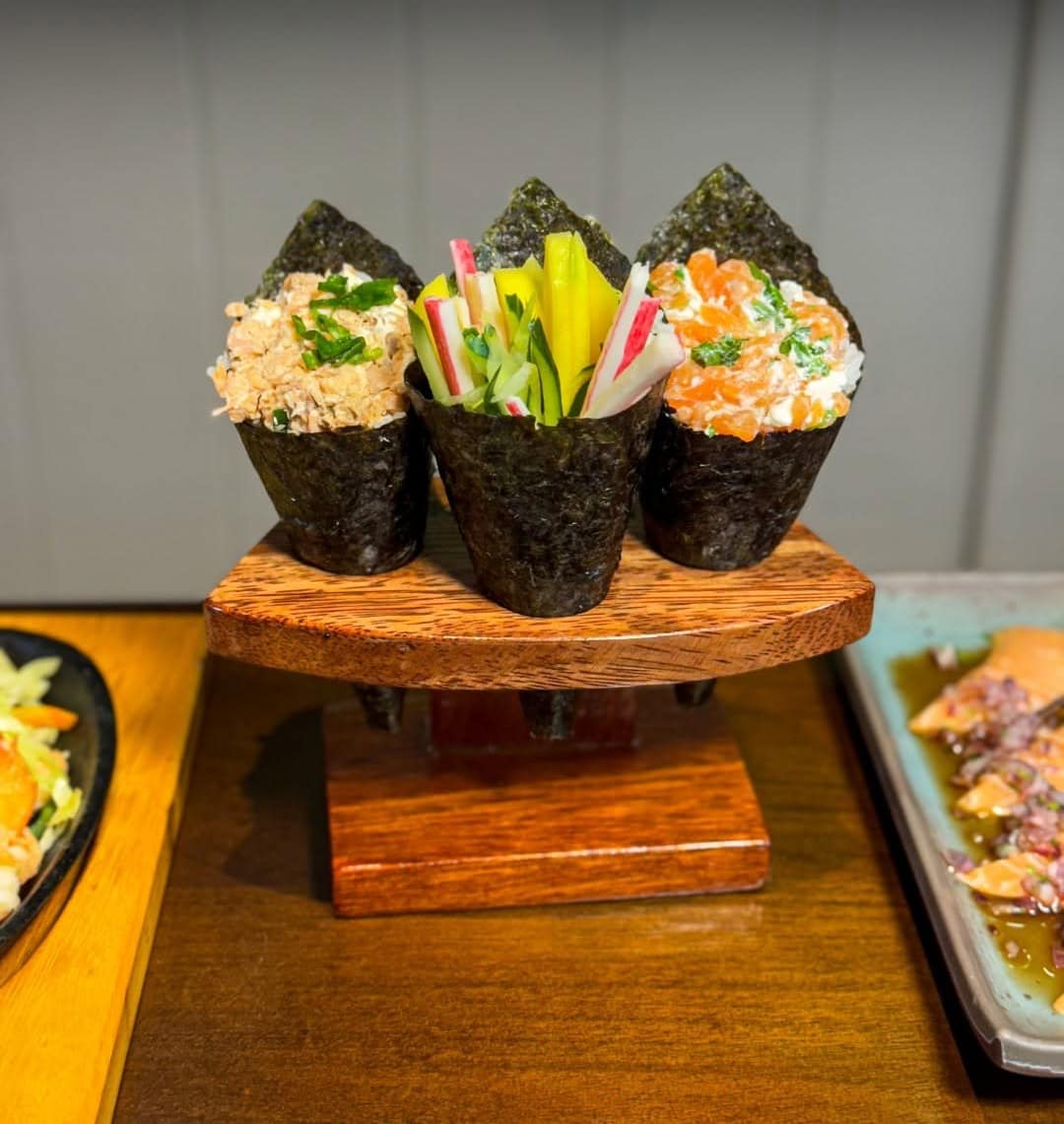 Temakis de salmão, kani e pepino num suporte de madeira